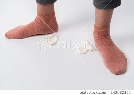 A small sock and a foot wearing a pink sock are lying on the floor. A small sock and a foot wearing a pink sock are lying on the floor. 142082363