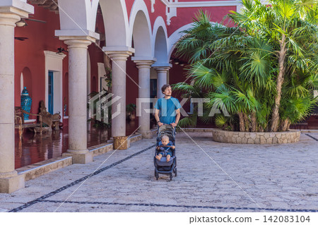 Man walking with baby stroller through Mexican colonial street, colorful architecture, heritage courtyard, fatherhood and family travel with baby concept Man walking with baby stroller through Mexican colonial street, colorful architecture, heritage courtyard, fatherhood and family travel with baby concept 142083104