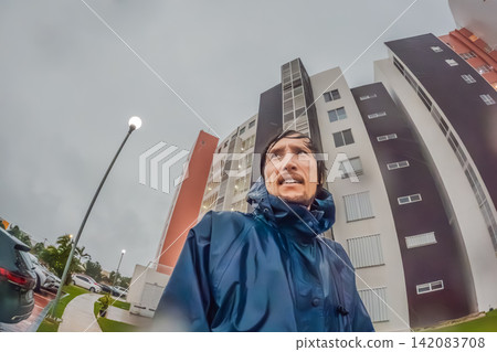 Adult man faces heavy rain and strong wind near palm trees and city buildings, showing storm weather, hurricane season and climate resilience concept Adult man faces heavy rain and strong wind near palm trees and city buildings, showing storm weather, hurricane season and climate resilience concept 142083708