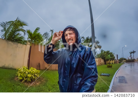Adult man faces heavy rain and strong wind near palm trees and city buildings, showing storm weather, hurricane season and climate resilience concept Adult man faces heavy rain and strong wind near palm trees and city buildings, showing storm weather, hurricane season and climate resilience concept 142083710