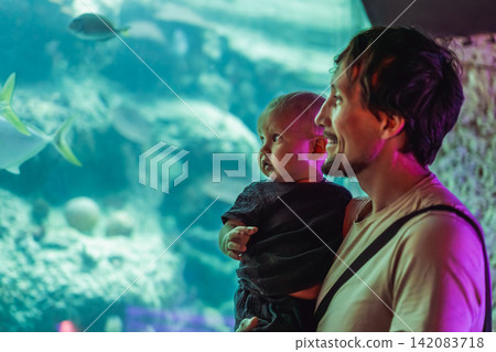 Man holding little baby while watching underwater world at aquarium, fatherhood, early learning, marine life discovery and family outing concept Man holding little baby while watching underwater world at aquarium, fatherhood, early learning, marine life discovery and family outing concept 142083718