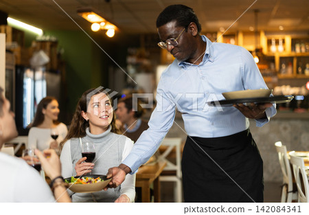 African man waiter serves cafe establishments girl visitor, puts food on table. African man waiter serves cafe establishments girl visitor, puts food on table. 142084341
