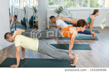 Group of people practicing various partner yoga positions during training in fitness studio Group of people practicing various partner yoga positions during training in fitness studio 142084696