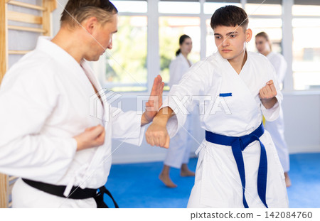 Young male attendee of karate classes fighting with middle-aged man in sports hall Young male attendee of karate classes fighting with middle-aged man in sports hall 142084760