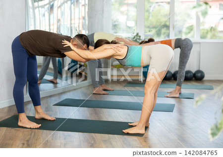 Women and men performing paired yoga exercises during group training at gym. Fitness and pair Hatha yoga concept. Women and men performing paired yoga exercises during group training at gym. Fitness and pair Hatha yoga concept. 142084765
