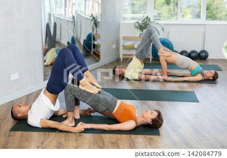 Young married couple meditate together in various yoga poses during group training in gym Young married couple meditate together in various yoga poses during group training in gym 142084779