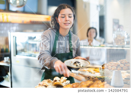 Young woman putting pastries on plate in cafe Young woman putting pastries on plate in cafe 142084791