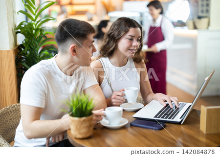 Girl and guy freelancers in cafe with laptop drinking coffee 142084878