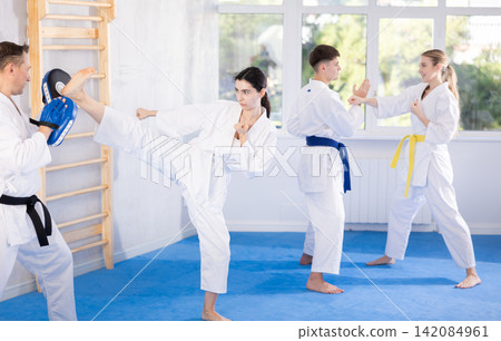 Young girl training kicks on punch mitts held by instructor 142084961