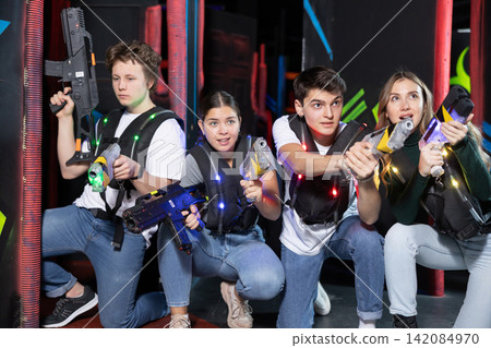 Four people having fun playing lasertag ducking behind cover in arena Four people having fun playing lasertag ducking behind cover in arena 142084970