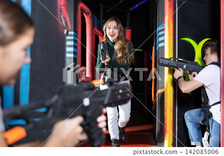 Smiling girl with laser pistol during playing laser tag with her friends in room 142085006
