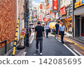 Pedestrians walk along narrow Sakae Dohri street lined with shops, izakaya bars, and signboards on a sunny summer day in Takadanobaba, Tokyo, Japan 142085695