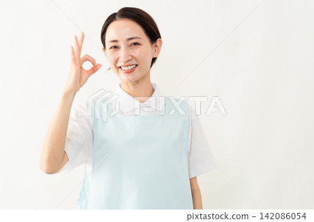A woman wearing a light blue apron; a caregiver image. A woman wearing a light blue apron; a caregiver image. 142086054