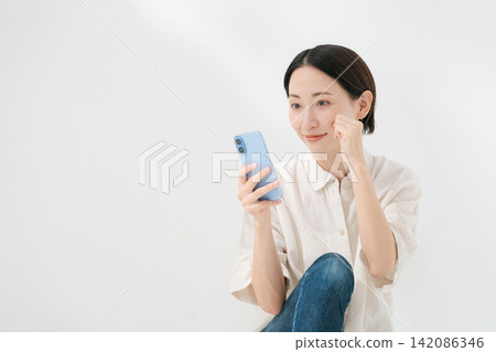 一位女士正透過智慧型手機的前置鏡頭看著自己的臉。 142086346