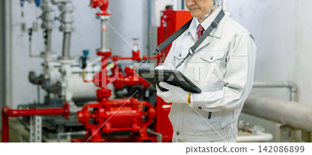 資深男性工人使用平板電腦檢查鍋爐房的設備。 資深男性工人使用平板電腦檢查鍋爐房的設備。 142086899