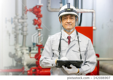 A senior male worker uses a tablet to inspect equipment in the boiler room. A senior male worker uses a tablet to inspect equipment in the boiler room. 142086907
