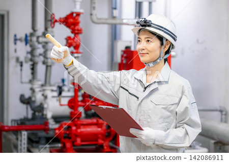 A female worker uses a tablet to inspect equipment in the boiler room. A female worker uses a tablet to inspect equipment in the boiler room. 142086911
