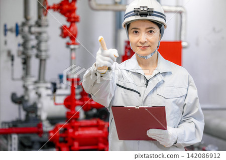 A female worker uses a tablet to inspect equipment in the boiler room. A female worker uses a tablet to inspect equipment in the boiler room. 142086912