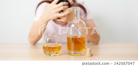 Stressed woman drinking whisky alone with problem. Exhausted drunk man looking stressed and sleepy. Alcohol addiction, Alcoholism, emotional distress and mental health concept Stressed woman drinking whisky alone with problem. Exhausted drunk man looking stressed and sleepy. Alcohol addiction, Alcoholism, emotional distress and mental health concept 142087047