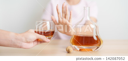 woman making stop hand gesture to refuse a glass of Cognac, Healthy man say no to alcohol drink, stop alcoholism and addiction concept. Responsible man reject a drink before driving and quit booze woman making stop hand gesture to refuse a glass of Cognac, Healthy man say no to alcohol drink, stop alcoholism and addiction concept. Responsible man reject a drink before driving and quit booze 142087052