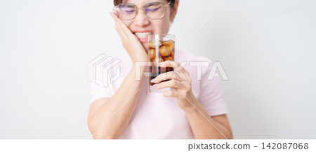 Woman drinking carbonated ice water and feeling sensitive teeth to cold pain, hand holding glass of cold sparkling water. dental health problem from soda acidity, toothache and oral care concept Woman drinking carbonated ice water and feeling sensitive teeth to cold pain, hand holding glass of cold sparkling water. dental health problem from soda acidity, toothache and oral care concept 142087068