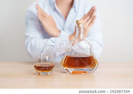Man making stop hand gesture to refuse a glass of Cognac, Healthy man say no to alcohol drink, stop alcoholism and addiction concept. Responsible man reject a drink before driving and quit booze Man making stop hand gesture to refuse a glass of Cognac, Healthy man say no to alcohol drink, stop alcoholism and addiction concept. Responsible man reject a drink before driving and quit booze 142087104