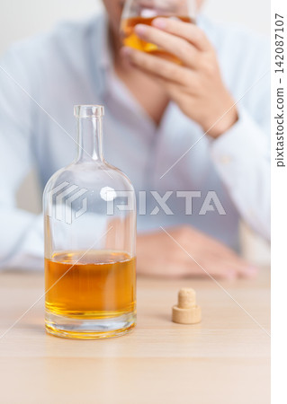 Stressed man drinking whiskey alone with problem. Exhausted drunk man looking stressed and sleepy. Alcohol addiction, Alcoholism, emotional distress and mental health concept Stressed man drinking whiskey alone with problem. Exhausted drunk man looking stressed and sleepy. Alcohol addiction, Alcoholism, emotional distress and mental health concept 142087107