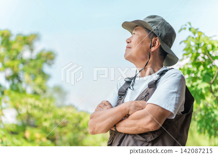 一位身著戶外服飾的老者置身於鬱鬱蔥蔥的森林中。 一位身著戶外服飾的老者置身於鬱鬱蔥蔥的森林中。 142087215