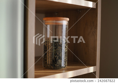 Glass jar with dried herbs on a wooden shelf 142087822