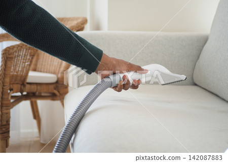 Cleaning a couch with a vacuum hose in a living room Cleaning a couch with a vacuum hose in a living room 142087883