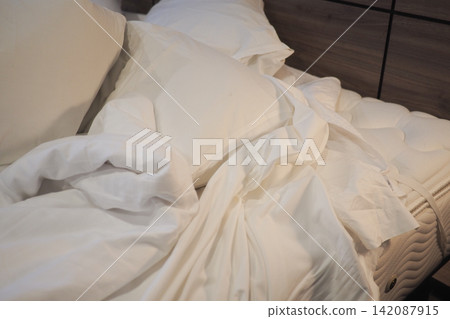 Messy bed with white sheets and pillows in a room 142087915