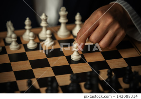 business hand moving a white pawn on wooden chessboard, strategy 142088314