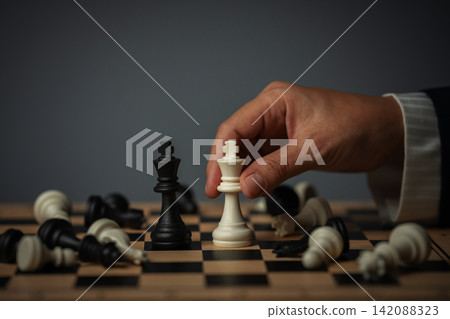 business hand placing white chess king facing off black on a board surrounded by pieces 142088323