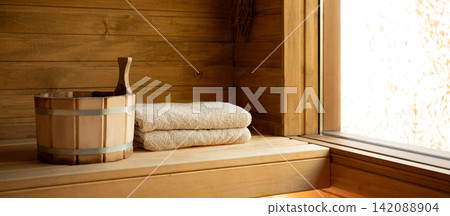 Wooden sauna interior features neatly folded towels and a wooden bucket Wooden sauna interior features neatly folded towels and a wooden bucket 142088904