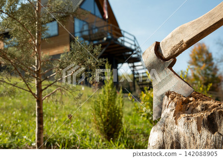Axe rests in tree stump in tranquil outdoor setting. Outdoor renovation and gardening concept Axe rests in tree stump in tranquil outdoor setting. Outdoor renovation and gardening concept 142088905
