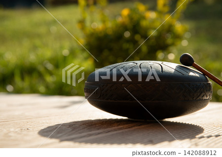 Tbilisi, Georgia - October 10, 2025: Handpan shines under sunlight on rustic table Tbilisi, Georgia - October 10, 2025: Handpan shines under sunlight on rustic table 142088912