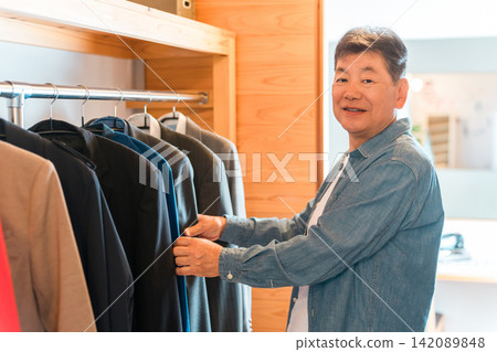 一位老年男子正在家裡的步入式衣櫥裡挑選衣服。 一位老年男子正在家裡的步入式衣櫥裡挑選衣服。 142089848
