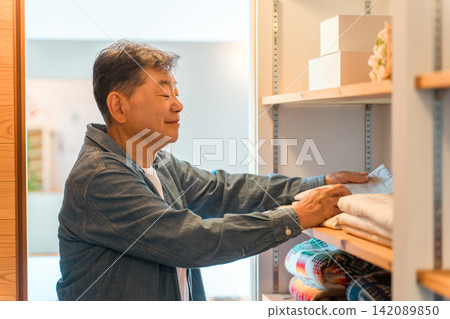 一位老年男子正在家裡的步入式衣櫥裡挑選衣服。 一位老年男子正在家裡的步入式衣櫥裡挑選衣服。 142089850