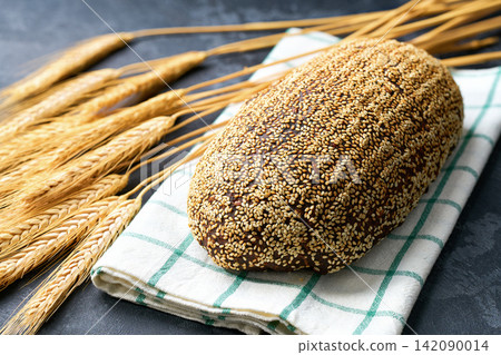 loaf wholemeal rye bread with sunflower seeds and sesame on dark kitchen table, selective focus. loaf wholemeal rye bread with sunflower seeds and sesame on dark kitchen table, selective focus. 142090014