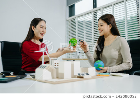 Engineers discuss eco-friendly city planning, holding green planet globes near solar and wind energy models. Engineers discuss eco-friendly city planning, holding green planet globes near solar and wind energy models. 142090052