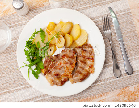 Fried pork served with potatoes and arugula Fried pork served with potatoes and arugula 142090546