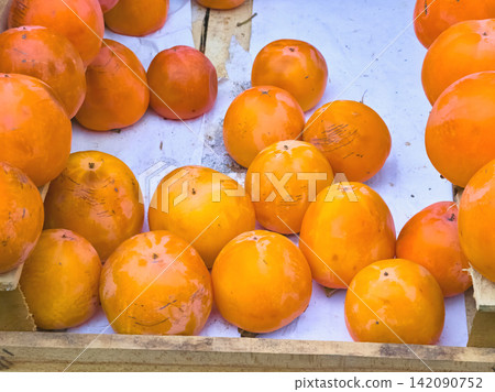 Orange ripe sweet juicy persimmon on market stall, delicious dessert Orange ripe sweet juicy persimmon on market stall, delicious dessert 142090752