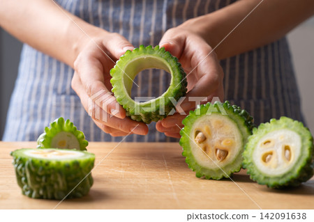 Woman hands removing seeds from a fresh bitter gourd, preparing food ingredient Woman hands removing seeds from a fresh bitter gourd, preparing food ingredient 142091638