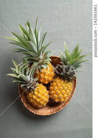 Fresh ripe pineapple in wicker basket on green cotton fabric background Fresh ripe pineapple in wicker basket on green cotton fabric background 142091661