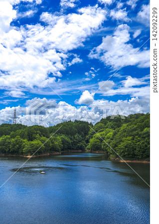 Summer clouds floating in the sky and the lake surface reflecting the blue sky; Nunome Dam; 35mm; blank copy space at the top; vertical composition; transmission tower on the left; suitable for web. Summer clouds floating in the sky and the lake surface reflecting the blue sky; Nunome Dam; 35mm; blank copy space at the top; vertical composition; transmission tower on the left; suitable for web. 142092299