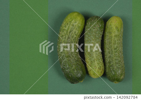 Three green gherkin cucumbers on green striped background Three green gherkin cucumbers on green striped background 142092784