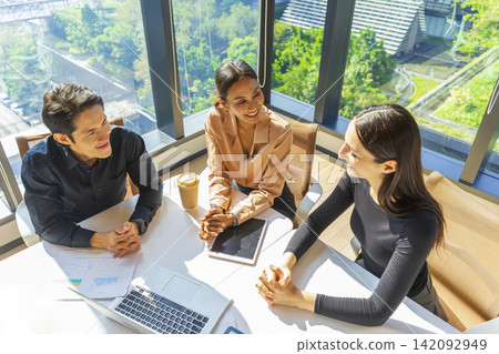 Caucasian businesswoman pointing to laptop screen while talking to her Asian coworker in office of a multinational company. Discussing work. 142092949