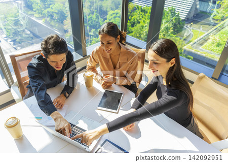 Caucasian businesswoman pointing to laptop screen while talking to her Asian coworker in office of a multinational company. Discussing work. 142092951