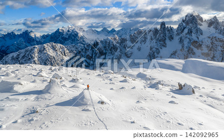 Ski mountaineer standing on a snowy rock in the Dolomites with wind blowing snow across alpine slopes, capturing winter adventure, solitude and dramatic mountain landscape. Ski mountaineer standing on a snowy rock in the Dolomites with wind blowing snow across alpine slopes, capturing winter adventure, solitude and dramatic mountain landscape. 142092965