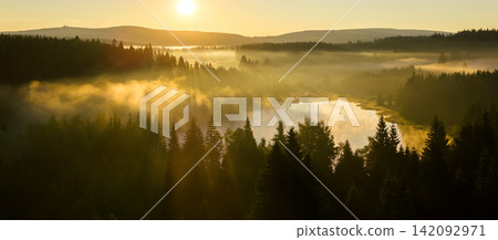 Golden sunrise over misty forest and lake in Northern Bohemia, Czech Republic. Morning fog, soft light, and tranquil atmosphere captured in high resolution perfect for fine art prints. Golden sunrise over misty forest and lake in Northern Bohemia, Czech Republic. Morning fog, soft light, and tranquil atmosphere captured in high resolution perfect for fine art prints. 142092971
